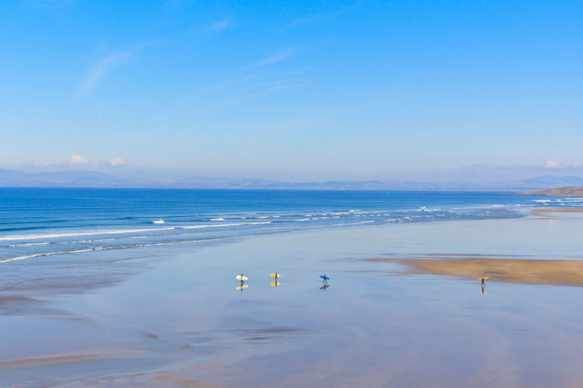 group of surfers walking on an empty beach in Bundoran Ireland