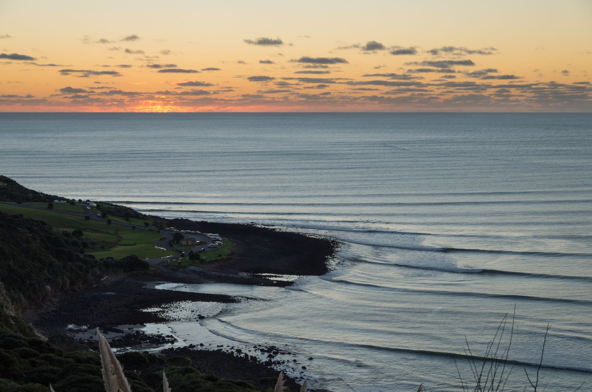 Group of surfers at Manu Bay in Raglan, New Zealand at sunset